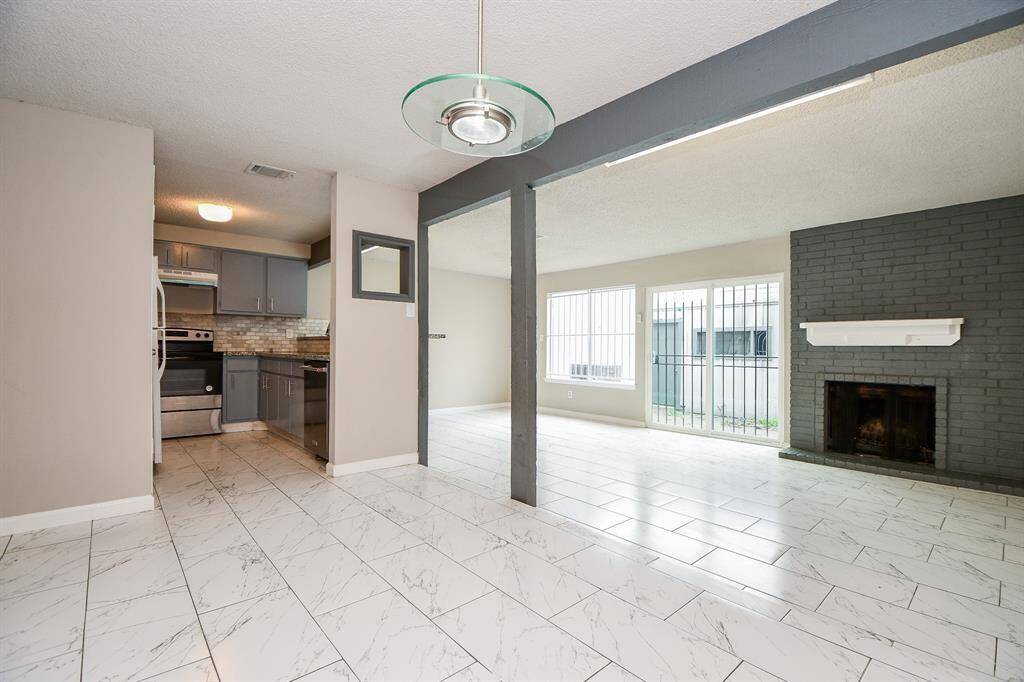 This photo showcases a bright, open-concept living area featuring large windows, a modern kitchen with stainless steel appliances, and a cozy fireplace. The space has sleek tile flooring and a contemporary design, perfect for comfortable living and entertaining.