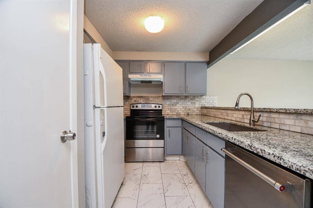 Modern kitchen with sleek granite countertops, stainless steel appliances, and light gray cabinetry. The space features a tiled backsplash and a clean, bright atmosphere.
