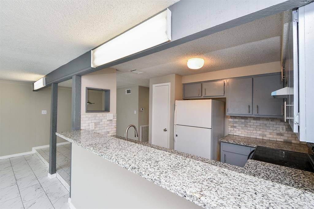 Modern kitchen with granite countertops, ample cabinet space, and a breakfast bar. Neutral tones and tile flooring create a bright, open atmosphere.