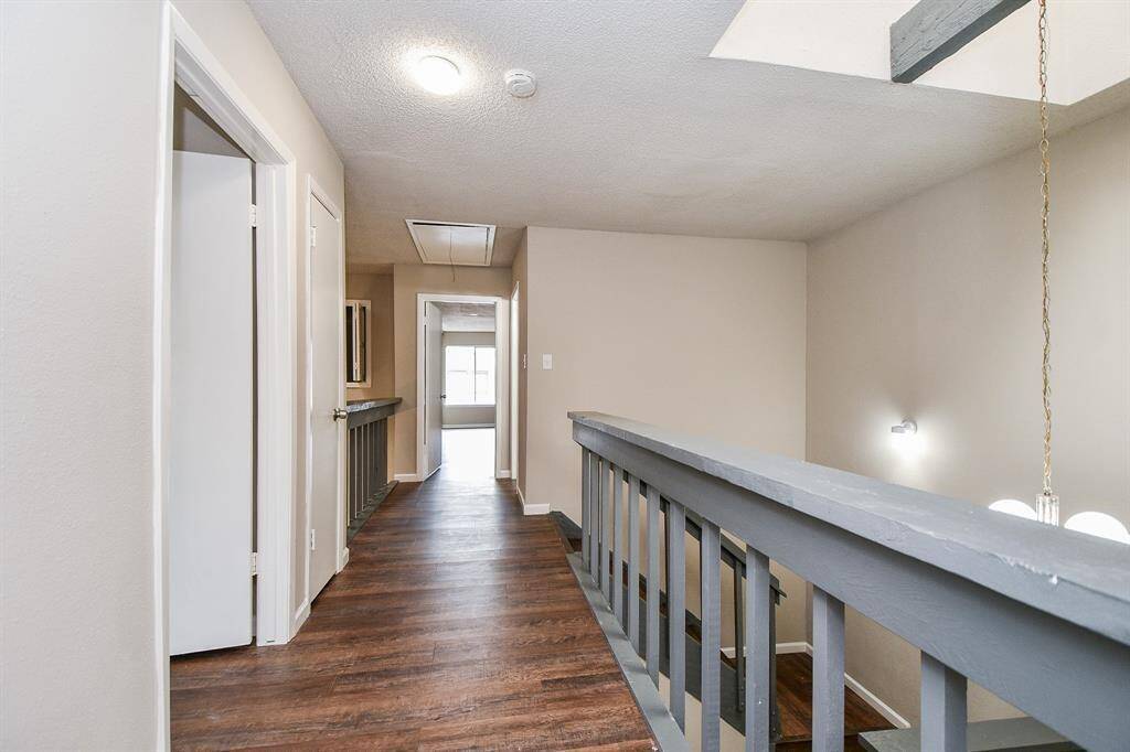 This photo shows a hallway with wood flooring, neutral walls, and a staircase railing. It leads to a bright room with a window at the end, offering a clean and open feel.