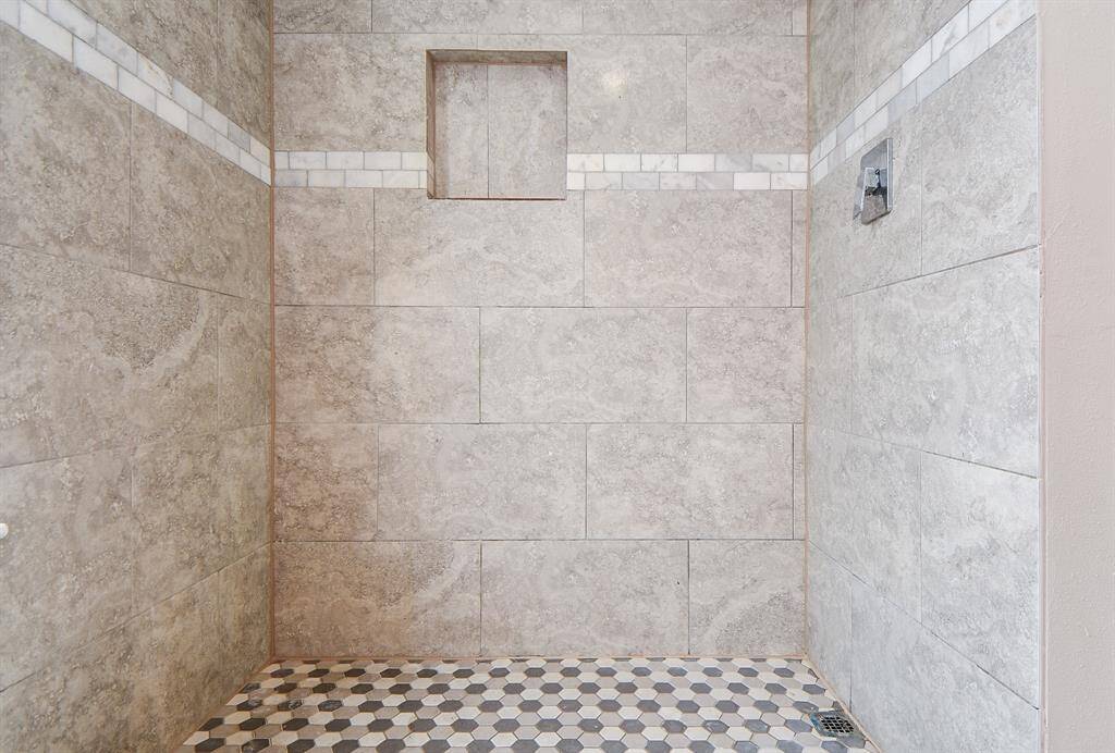 Spacious shower with elegant stone tiles, featuring a built-in niche and stylish hexagonal floor tiles. Perfect for a modern bathroom.