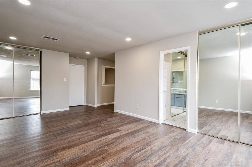 Spacious room with hardwood flooring, neutral walls, and recessed lighting. Features mirrored sliding closet doors and an attached bathroom, creating a modern, open feel.