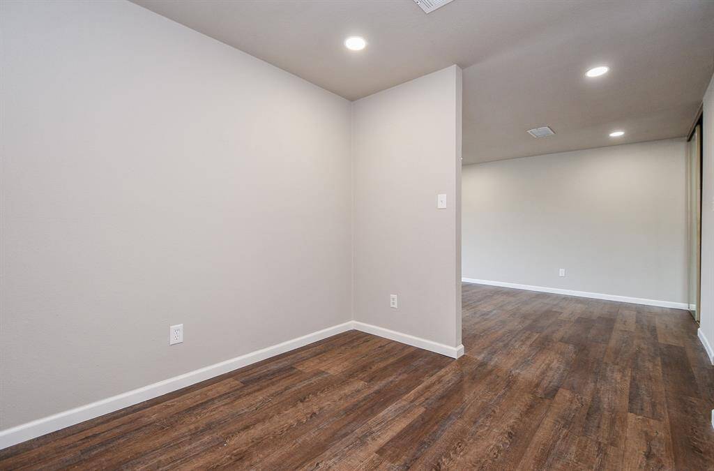 This photo shows a bright, open hallway with wood flooring, recessed lighting, and neutral-colored walls, offering a modern, spacious feel.