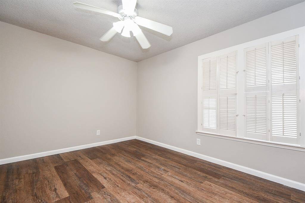 This room features neutral walls, wood flooring, and a ceiling fan. A window with shutters provides natural light, creating a bright and inviting space.