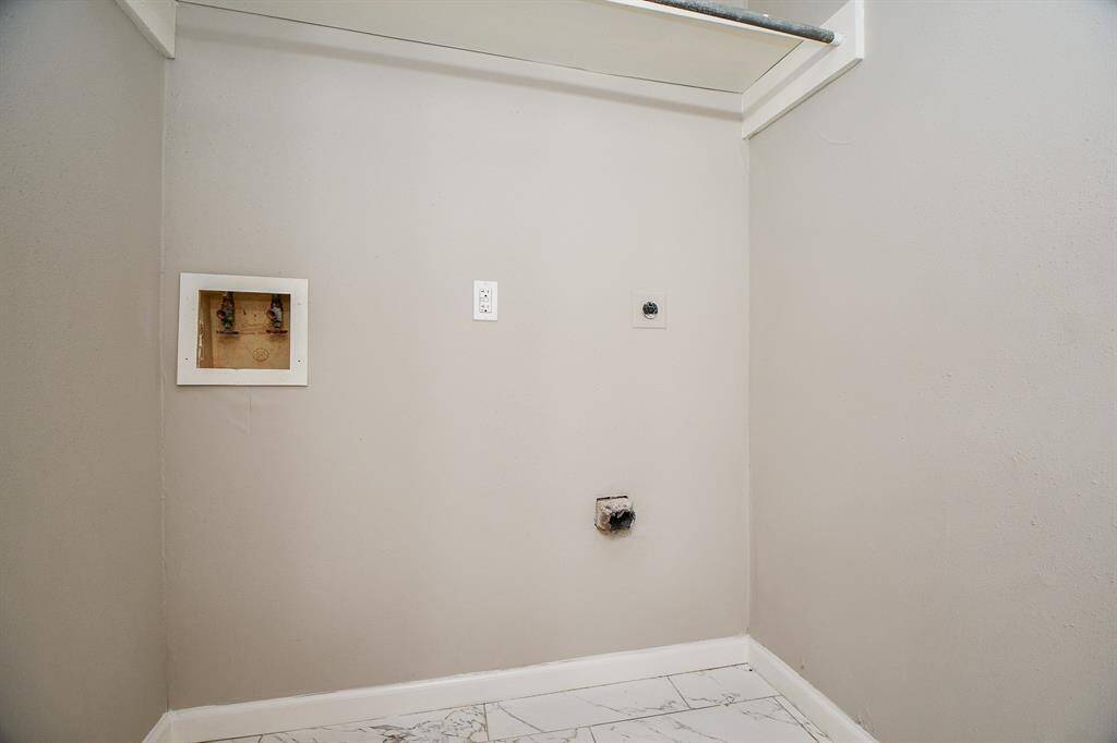 This photo shows a laundry area with hookups for a washer and dryer. It features light-colored walls and tiled flooring, providing a clean and functional space for laundry appliances.