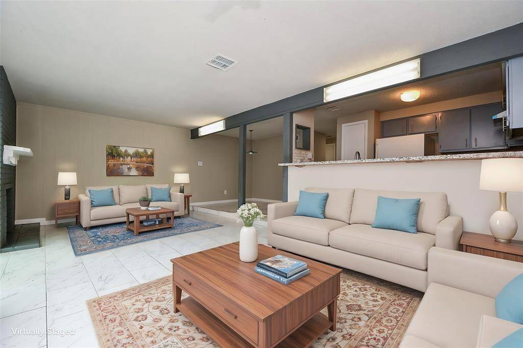 This virtually staged photo showcases a spacious, open-concept living area with modern furnishings and neutral colors. It features a cozy seating arrangement, a fireplace, and a view into the kitchen, creating a warm and inviting atmosphere. Virtual staging was used.