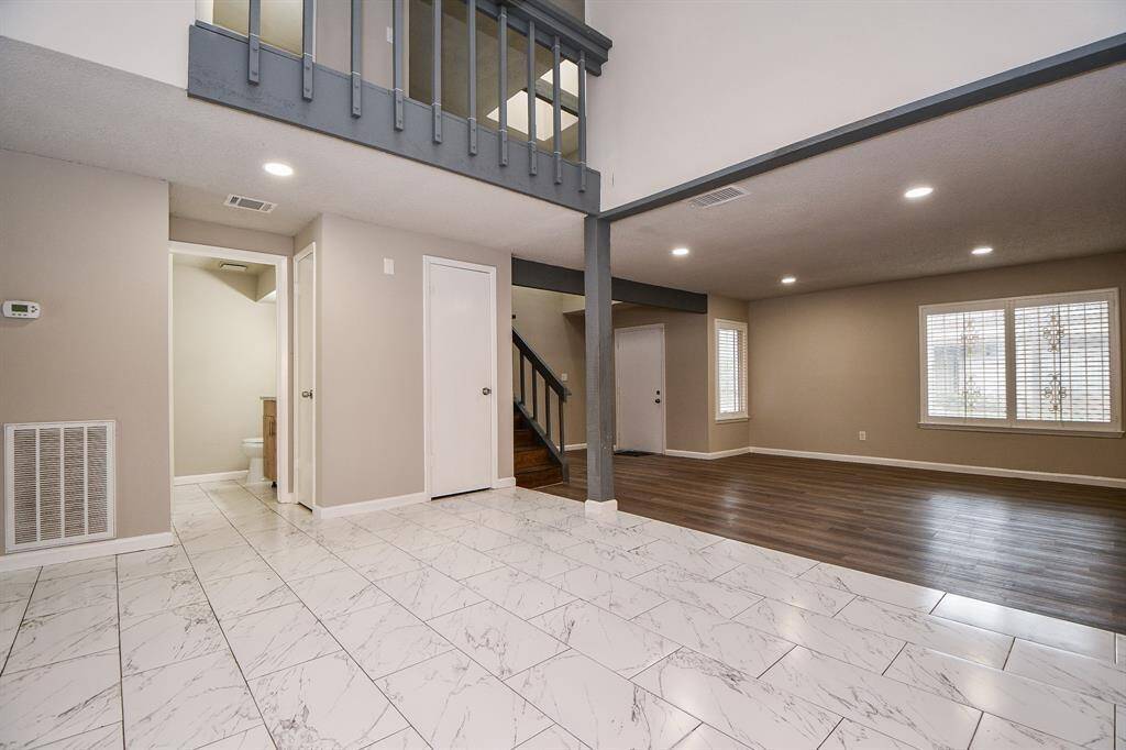 This spacious living area features a modern open layout with high ceilings, a mix of marble and wood flooring, and ample natural light from large windows. An upstairs loft overlooks the main space, adding a touch of elegance.