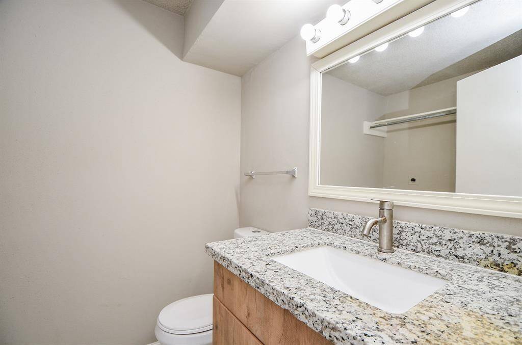This bathroom features a modern granite countertop with an under-mount sink, a sleek faucet, and a large framed mirror with overhead lighting. The neutral walls create a clean and spacious feel.