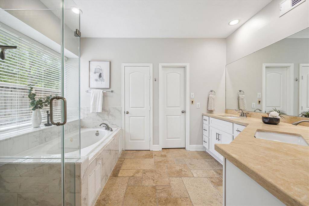 With dual sink vanities, white cabinetry, travertine countertops, frameless glass shower and separate jetted tub. The door to the right opens to a spacious walk-in closet.