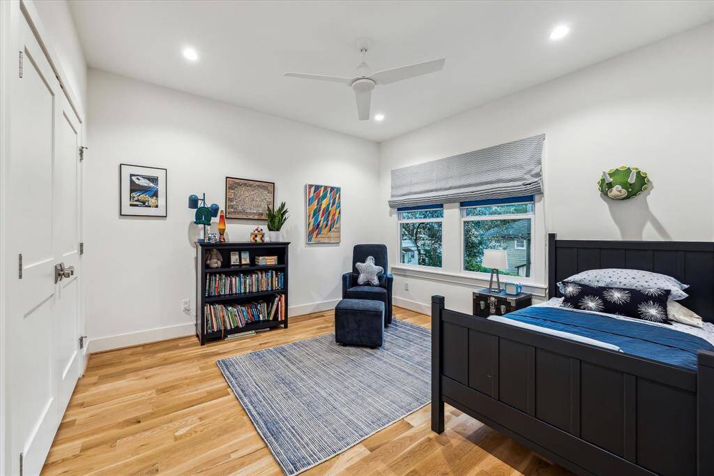 Secondary bedroom with white oak floors, closet with built-ins, recessed lighting, ceiling fan and custom shades with black out curtains.