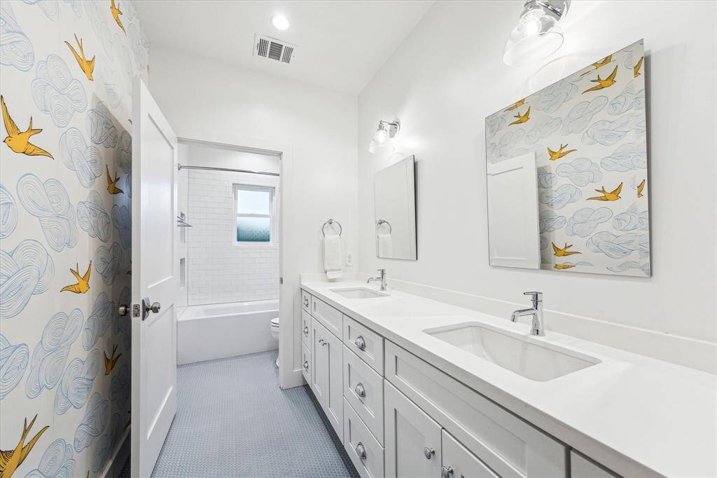 Full bathroom for the two secondary bedrooms upstairs with quartz counters, double sinks, stylish wallpaper, a shower/tub combo and light blue penny tile.