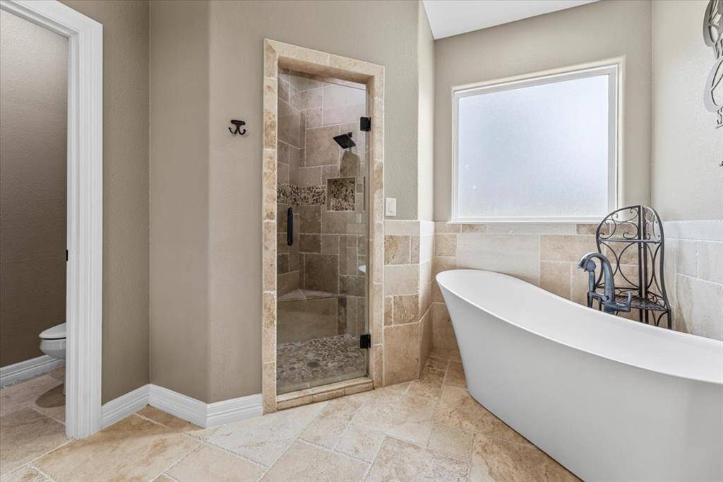 This bathroom features a modern design with a freestanding soaking bathtub, a glass-enclosed shower with stone tile accents, and a frosted window for natural light and privacy.