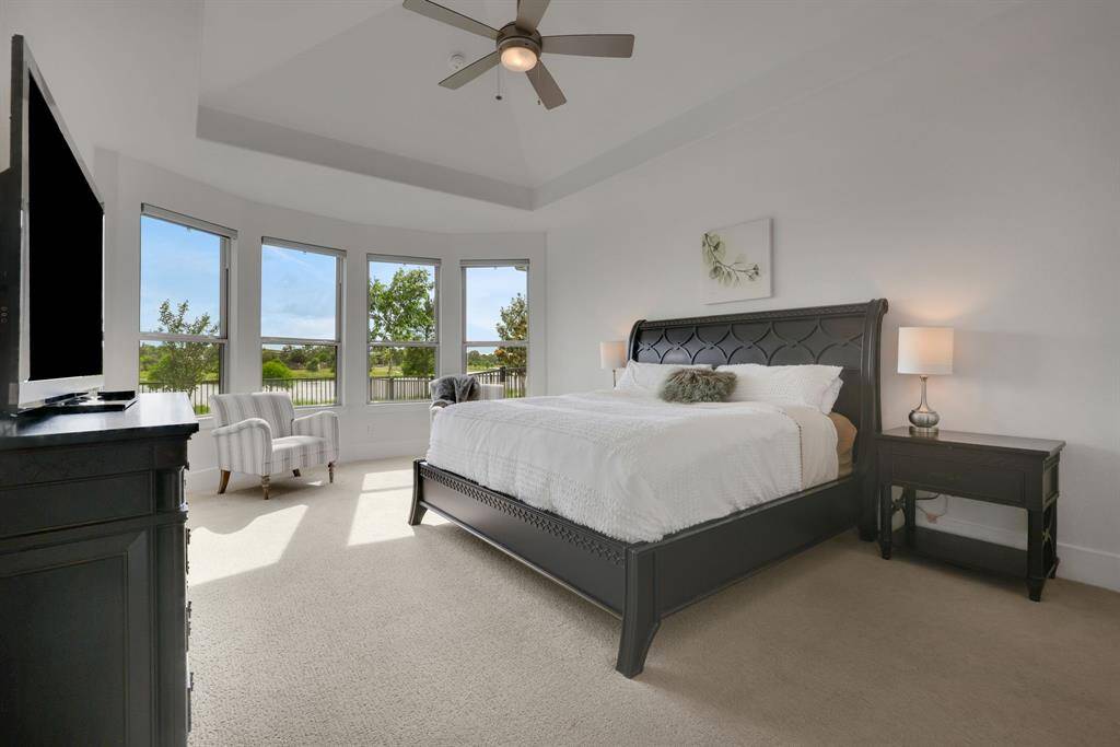 The large primary suite complete with ceiling fan, trayed ceiling detail, and lake views.