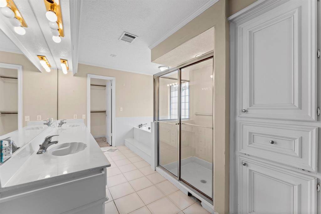 Spacious bathroom with dual sinks, a large mirror, and ample lighting. Features a glass-enclosed shower, built-in storage cabinets, and a separate bathtub. Neutral tones create a bright, clean atmosphere.