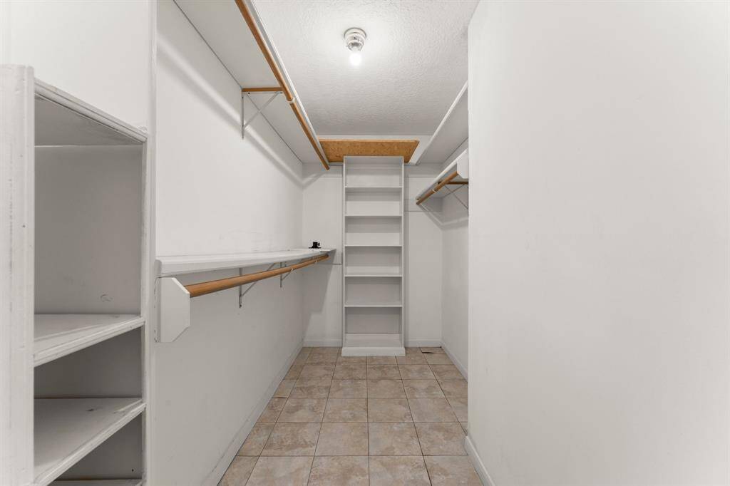Spacious walk-in closet with ample shelving and hanging space, tiled floor, and a central light fixture. Perfect for organized storage.