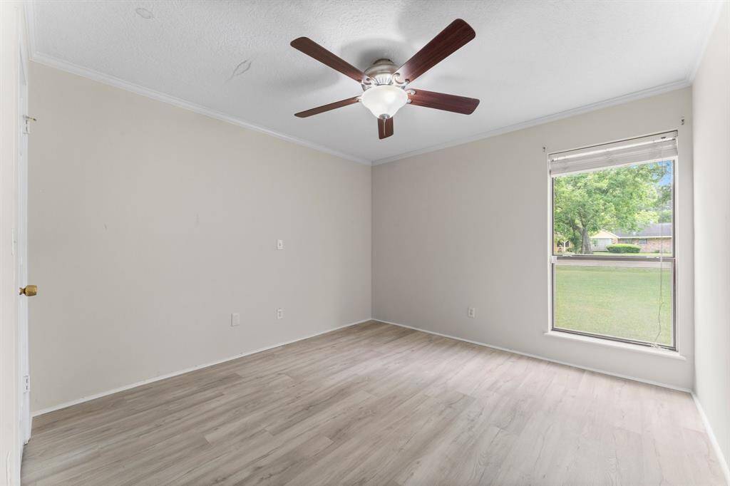 This room features neutral walls, light wood flooring, and a ceiling fan. A large window offers plenty of natural light and a view of the front yard.