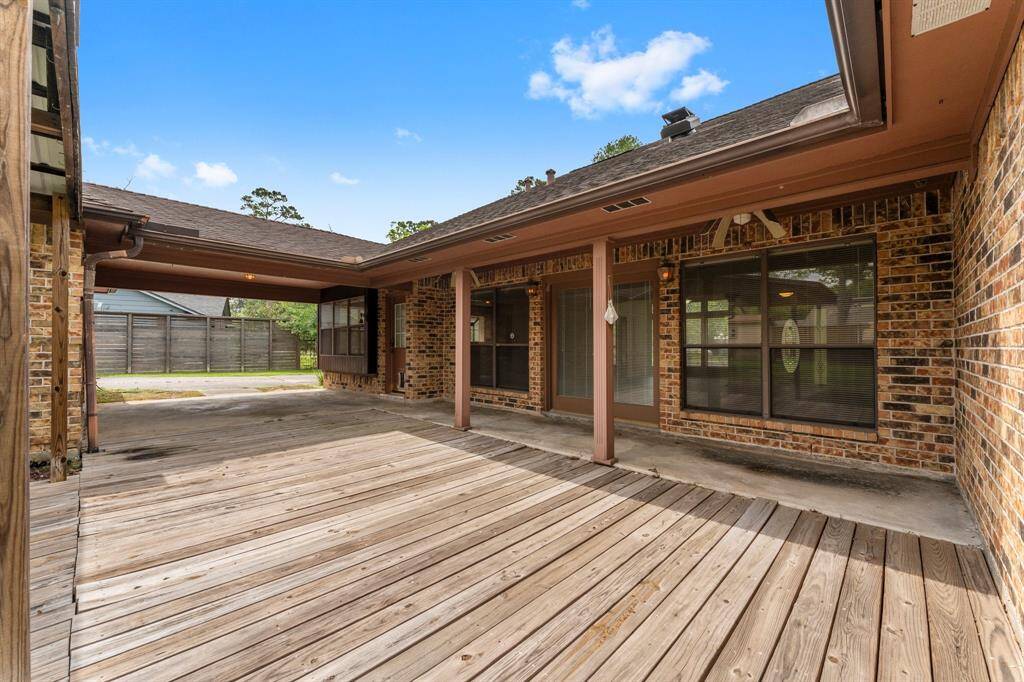 This photo showcases a spacious backyard patio with a wooden deck, ideal for outdoor gatherings. The area is partially covered, providing shade, with large windows and brick exterior walls enhancing its charm.