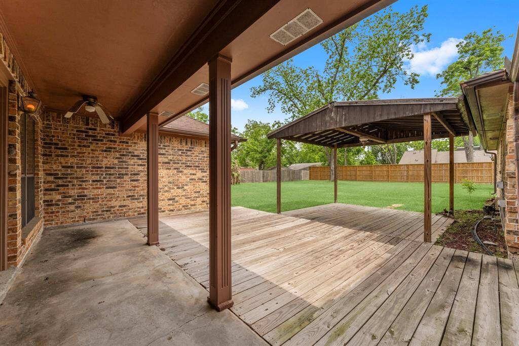 Spacious backyard with a covered patio and wooden deck, perfect for outdoor gatherings. The area features a well-maintained lawn and privacy fencing, offering a serene and private outdoor space.