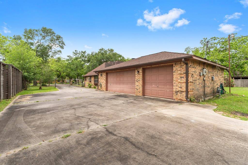 Spacious driveway leading to a brick garage with dual doors, surrounded by lush greenery and a fenced yard. Ideal for multiple vehicles and outdoor activities.