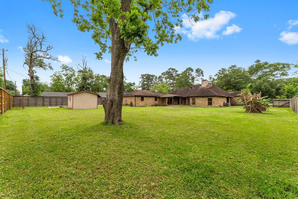 Spacious backyard with a large lawn, mature trees, and a small shed. The brick house has a covered patio and is surrounded by a wooden fence, providing privacy and a serene setting.