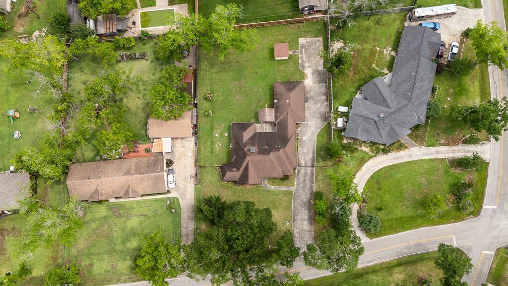 This aerial view showcases a property with a spacious yard, mature trees, and a long driveway leading to the house. Adjacent homes provide a sense of neighborhood, and the surrounding greenery adds privacy and charm.
