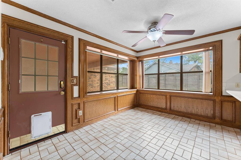 This bright sunroom features large windows, wood paneling, and a ceiling fan, offering a cozy space with ample natural light. The tiled floor complements the warm wooden accents, creating a welcoming atmosphere.