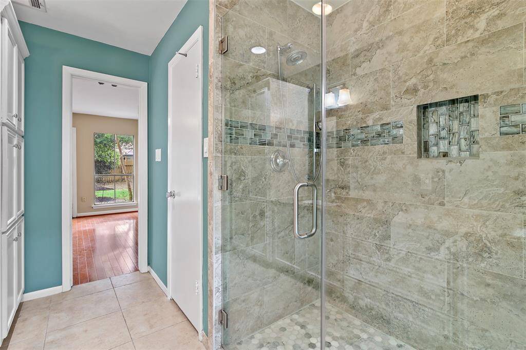 Updated primary bathroom features a walk in glass shower with decorative tile inlay.