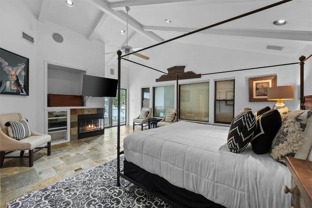 This luxurious primary bedroom features vaulted ceilings, a cozy fireplace, and large windows that frame serene water views.