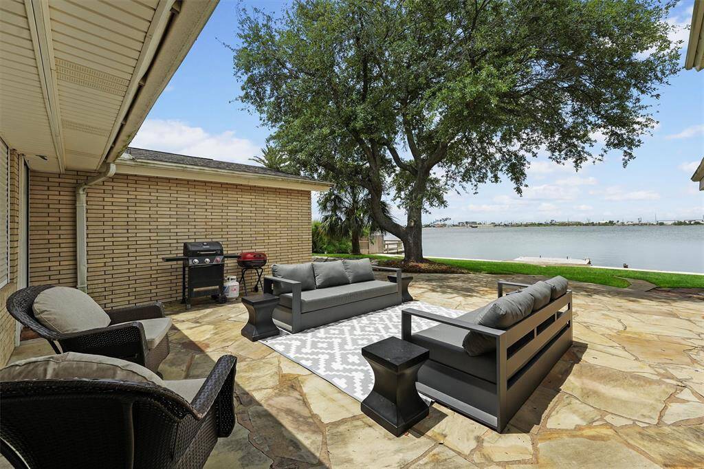 Enjoy outdoor living in this open-air seating area with a grill and beautiful water views, all shaded by a large tree for ultimate relaxation.