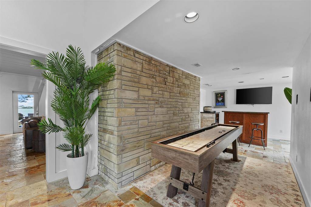 This cozy space features a shuffleboard table, stone accent wall, bar seating, and warm lighting—perfect for laid-back fun.