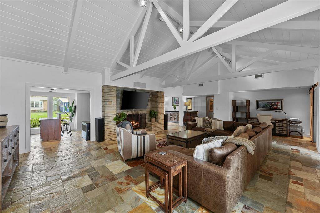 This expansive living room impresses with soaring white beam ceilings, a roomy sectional, and a statement stone fireplace offering plenty of space to relax or entertain.