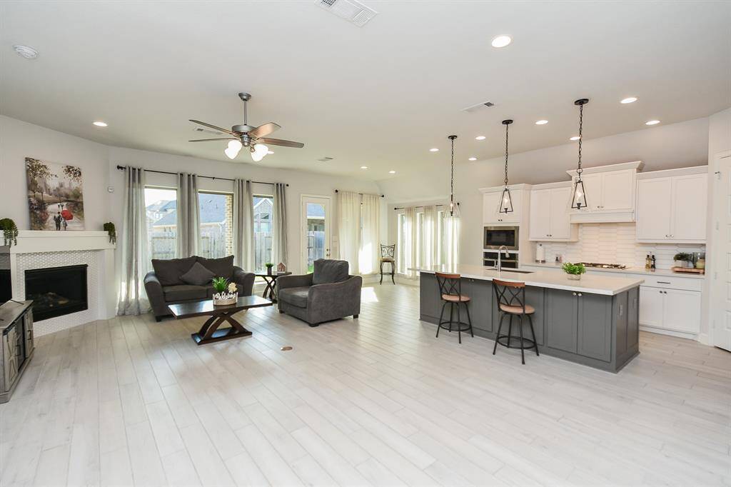 This spacious open-concept living area features a modern kitchen with a large island, pendant lighting, and ample white cabinetry. The adjoining living room has a cozy fireplace, large windows for natural light, creating an inviting atmosphere.