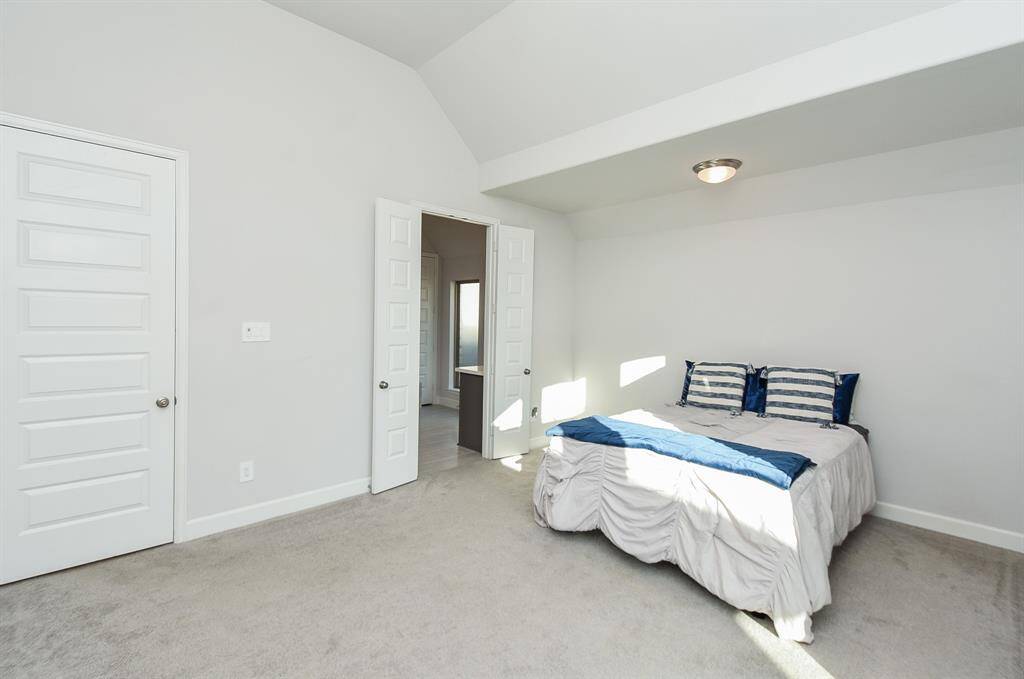 This photo shows a bright, spacious bedroom with neutral walls and carpet. Double doors lead to the primary bathroom and closet spaces.