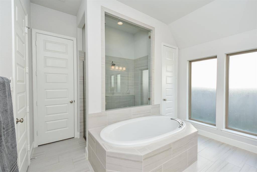 Bright and spacious bathroom featuring a large soaking tub, glass-enclosed shower, and frosted windows for privacy. The neutral color palette and modern fixtures create a serene and inviting atmosphere.