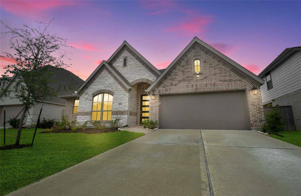 This photo showcases a charming brick home with a two-car garage and a well-maintained front yard. The house features large, inviting windows and is set against a picturesque sunset sky, creating a welcoming atmosphere.
