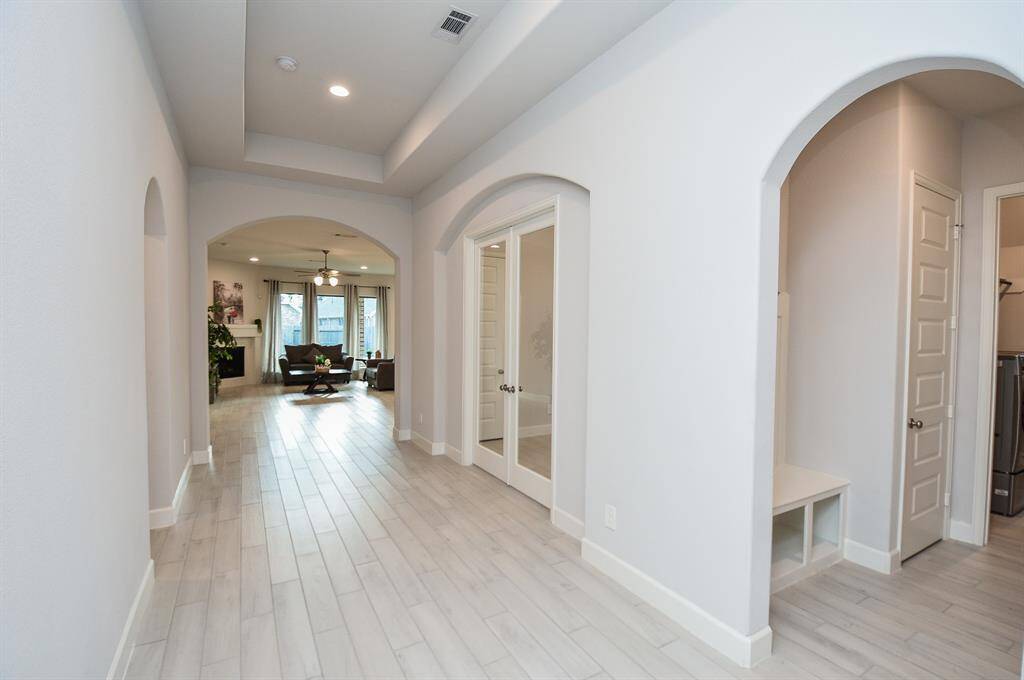 This photo showcases a bright, spacious hallway with elegant archways leading to a cozy living area with a ceiling fan and large windows, allowing natural light to fill the space.
