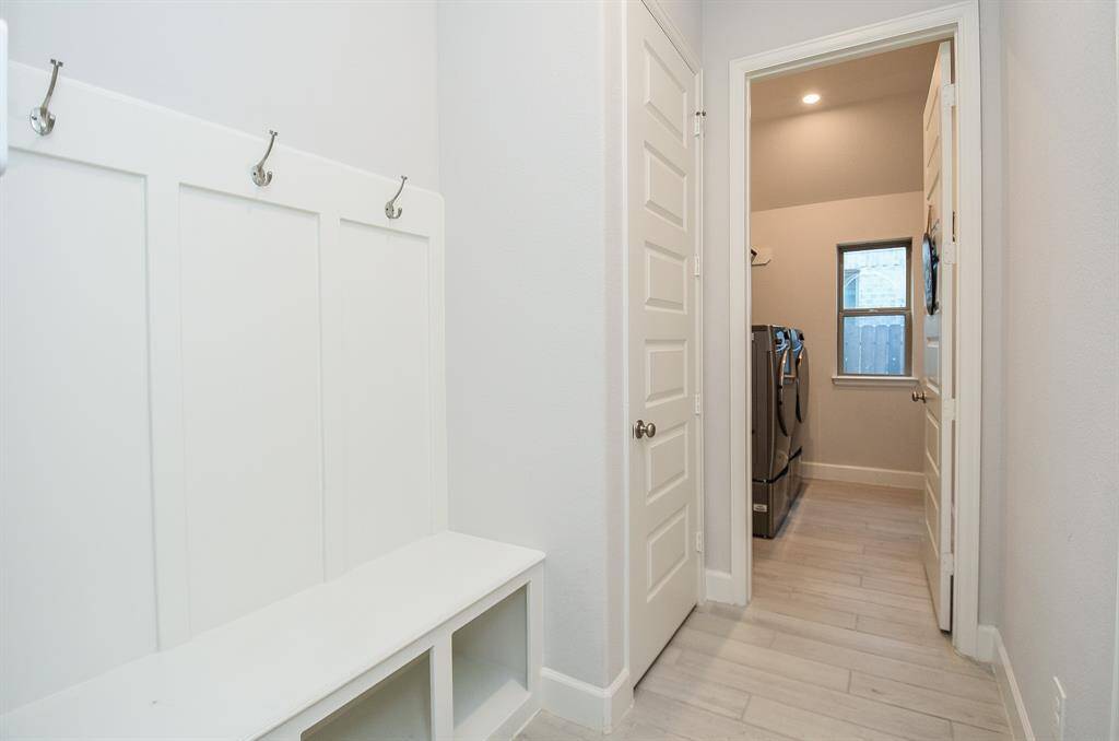 This photo features a bright and functional mudroom with built-in storage and coat hooks. It leads into a spacious laundry room with modern appliances and a window for natural light. The space is clean and well-organized, ideal for everyday convenience.