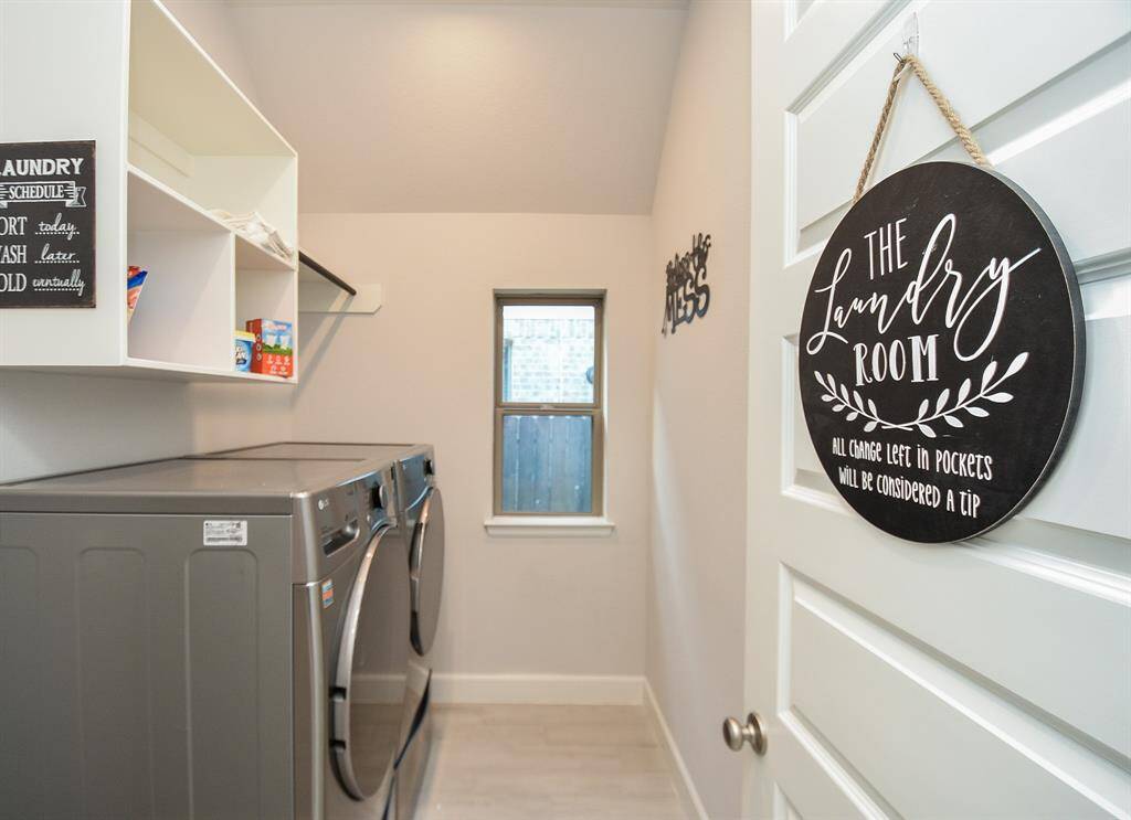 This is a well-organized laundry room featuring modern appliances, open shelving for storage, and a window for natural light. It has a light, neutral color scheme and playful decor for a welcoming atmosphere.
