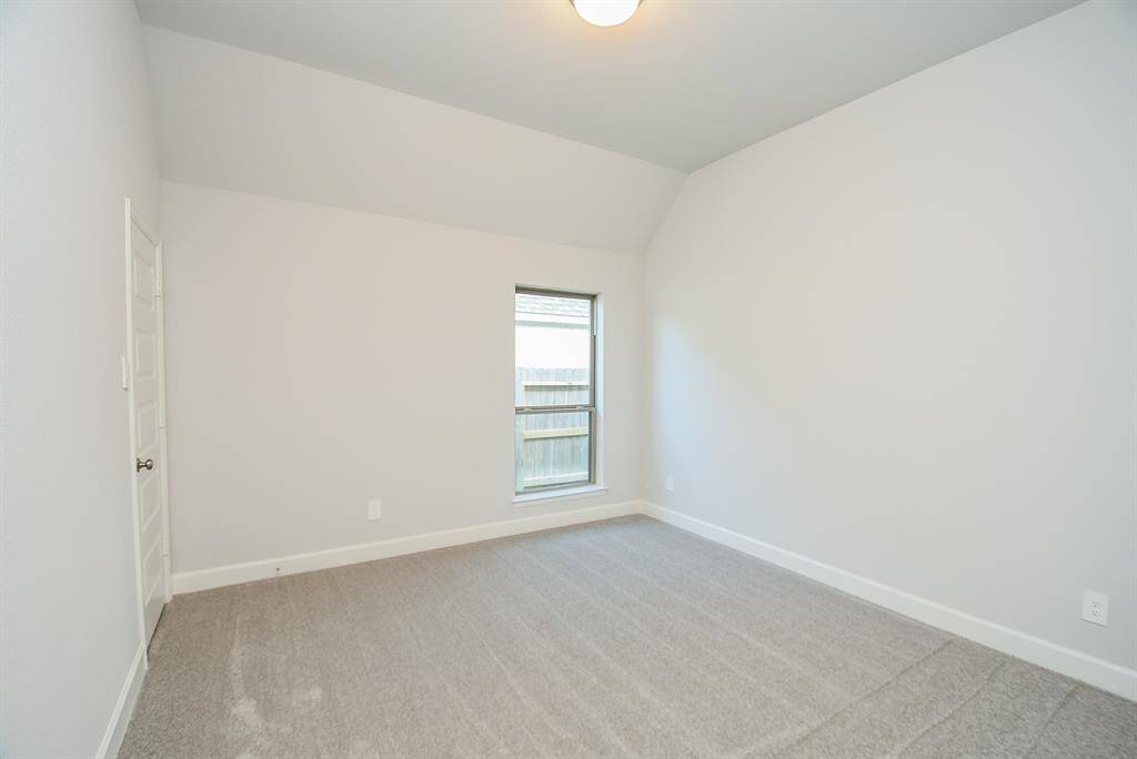This room features neutral-colored walls and carpet, a single window providing natural light, and a simple ceiling light fixture, offering a clean, versatile space.