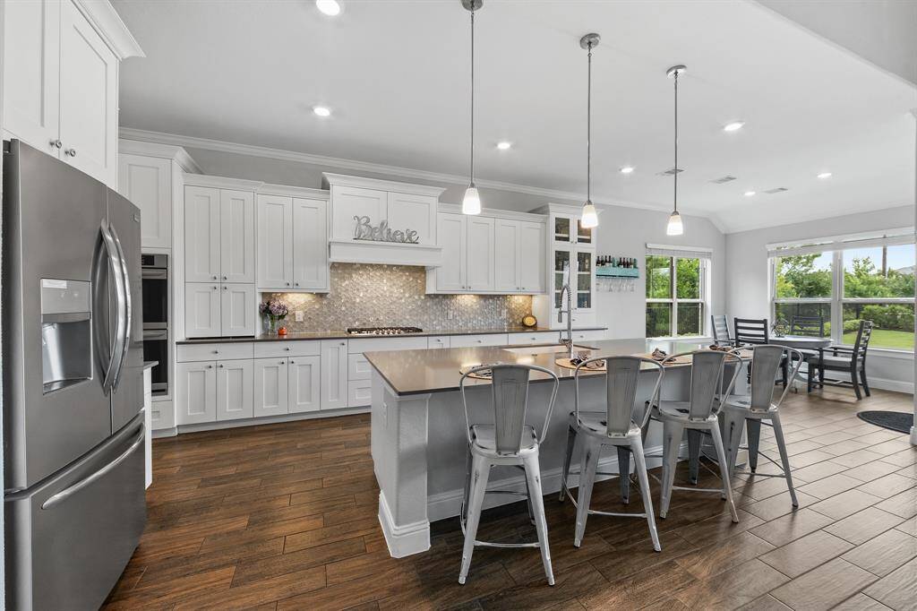 White cabinetry surrounds the huge island, complemented by beautiful light fixtures and farmhouse sink that elevate the overall aesthetic and create a bright, inviting atmosphere.