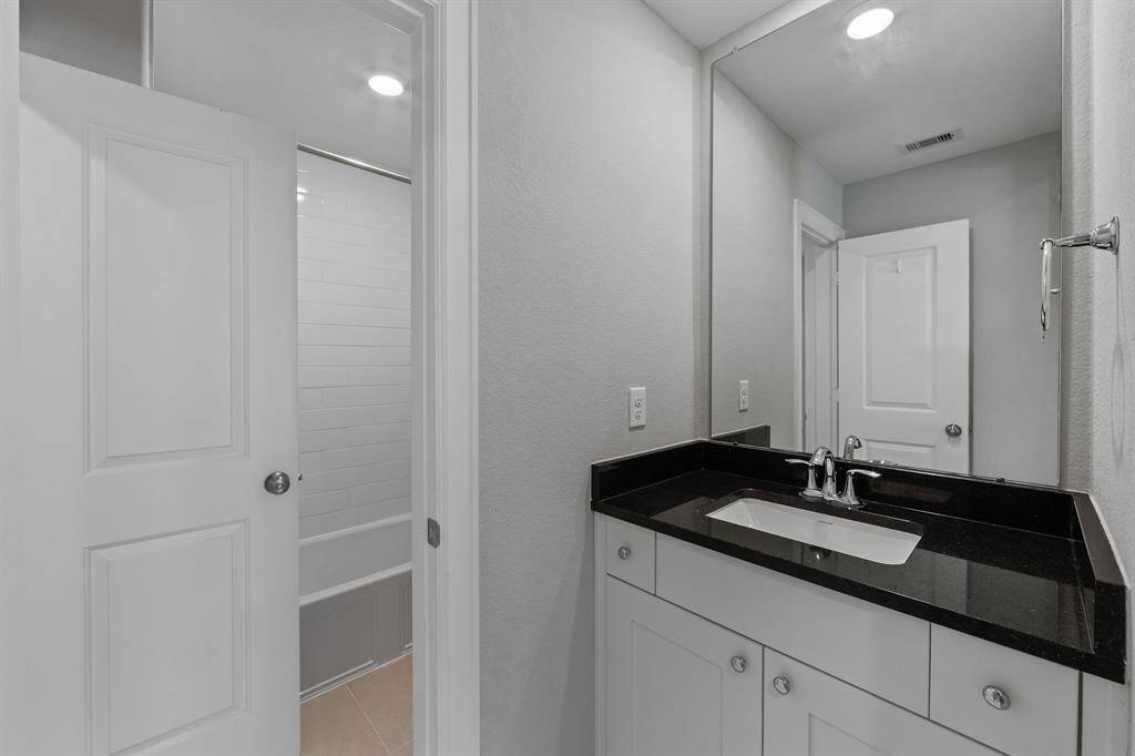 This secondary bathroom offers a tub and shower combo, complemented by a black glass countertop and a single-sink vanity. White cabinets add a clean, modern touch, balancing the bold finishes with classic elegance.