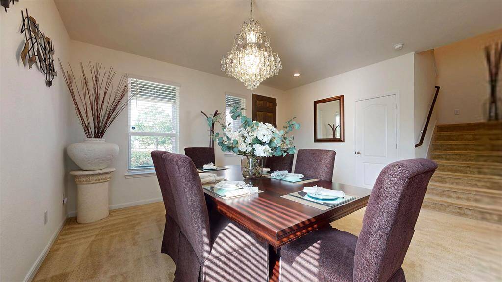 Another view of the dining area, with windows that allow natural light and a view of the wide staircase on the right and the front door ahead.