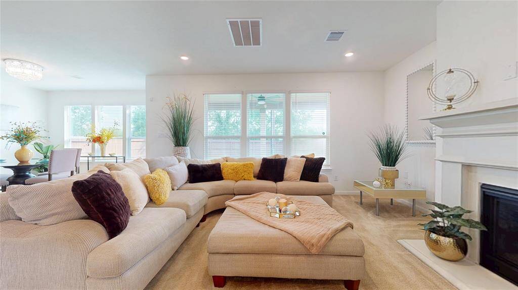 This spacious and inviting living room has a cozy fireplace, a high ceiling, and abundant natural light from multiple windows. The neutral tones and tasteful decor create a warm, welcoming atmosphere, perfect for relaxation and entertaining.