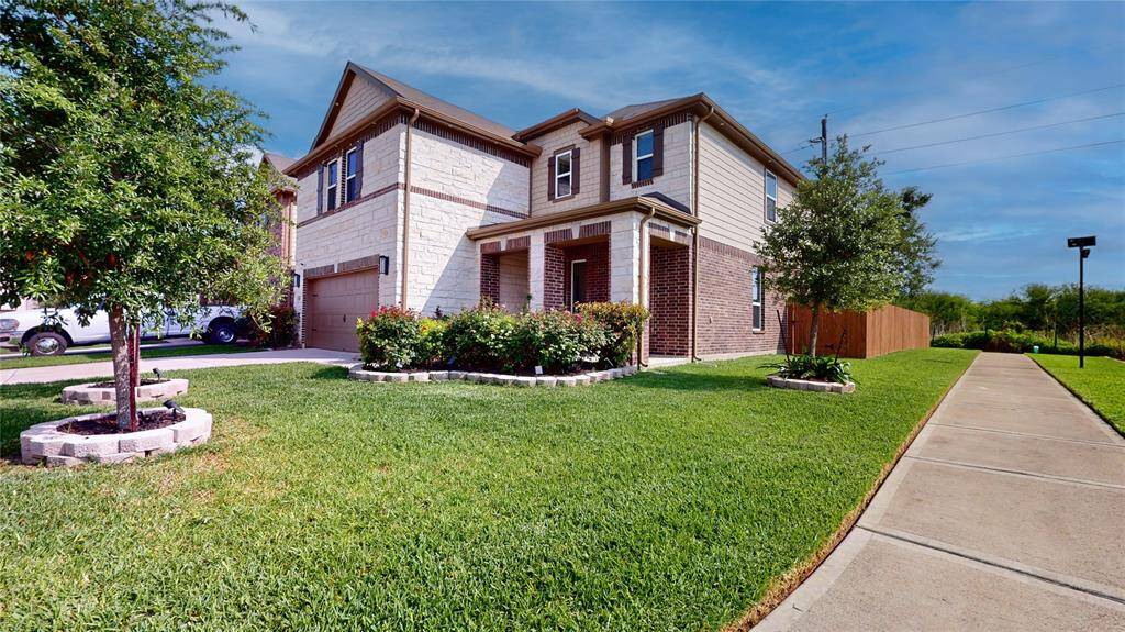 This is a modern two-story home with a stone and brick exterior. It has a well-maintained lawn, a two-car garage, and a welcoming front porch with landscaped trees and shrubs.