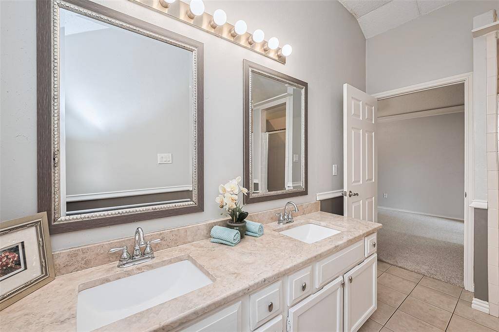 The spa-like bathroom includes double vanities, granite countertops, framed mirrors, and ample cabinet storage.