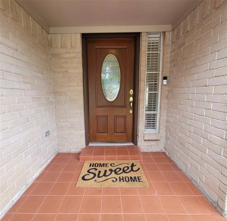 Cozy covered porch entrance with a wooden door accented by a decorative oval glass insert.