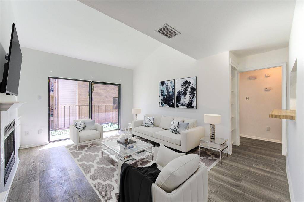 This elegant living room offers an open layout with vaulted ceilings and abundant natural light. A sleek fireplace adds warmth, while luxury vinyl plank flooring and contemporary décor enhance the modern appeal. The seamless flow to the balcony makes it perfect for relaxing or entertaining.