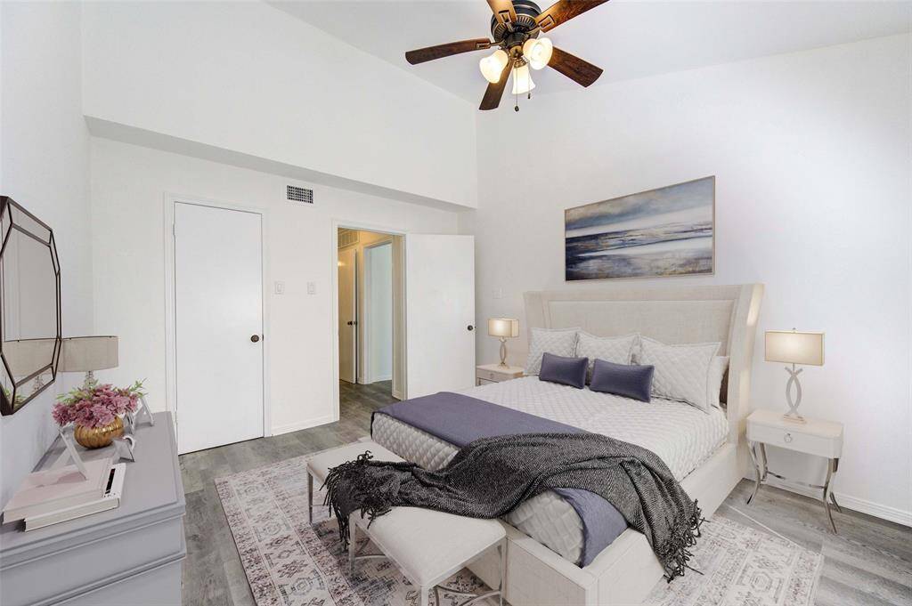 This serene bedroom features soaring ceilings, soft neutral tones, and a spacious layout designed for comfort. The plush upholstered bed, elegant nightstands, and calming artwork create a peaceful retreat. Luxury vinyl plank flooring and stylish accents add a modern touch, while warm lighting enhances the inviting atmosphere.