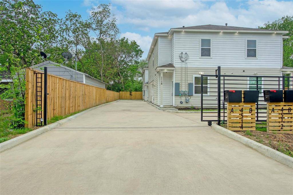 This photo shows a modern two-story home with a clean, white exterior. It features a spacious driveway and is surrounded by a wooden fence, offering privacy. The area is well-maintained with some greenery, providing a pleasant outdoor space.