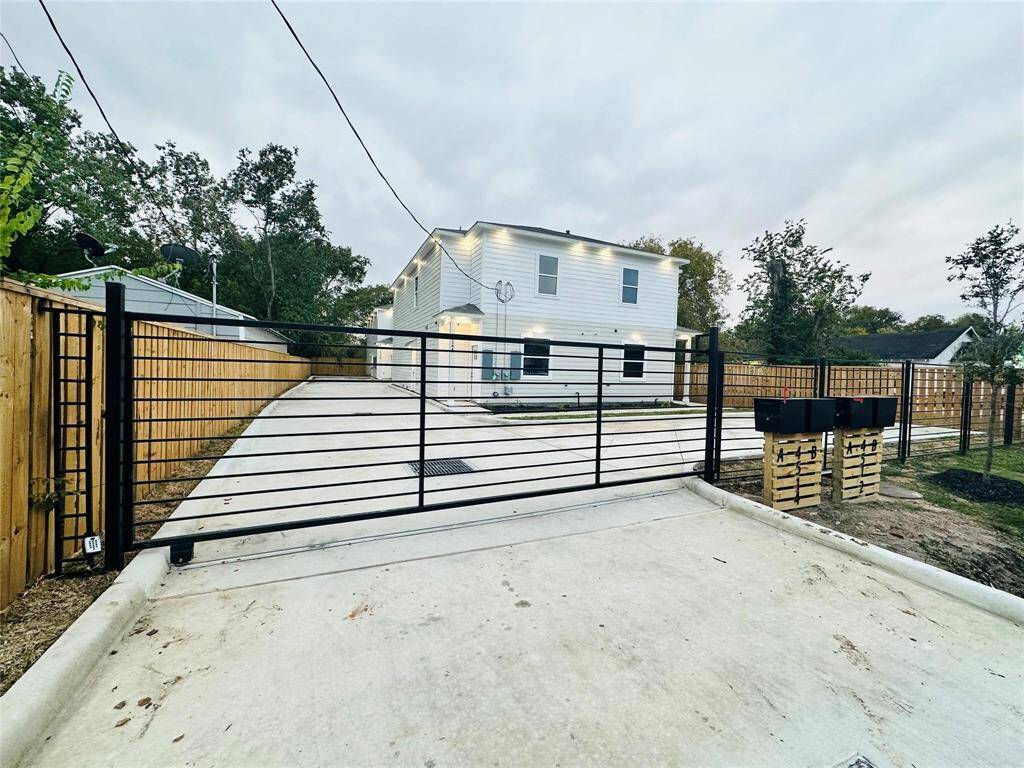 Modern two-story home with a gated driveway for added security. The exterior features clean, white siding and large windows. The property includes multiple mailboxes. Surrounded by trees, it offers a sense of privacy.